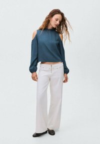 Bluză lungă cu mânecă în teal, cu design cu umeri descoperiți și model texturat, combinată cu pantaloni albi cu talie înaltă și croială largă. Pantofi negri cu puncte.