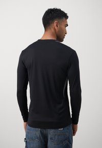 Zwarte langemouwenshirt met een gladde textuur, ronde halslijn en zijpaneelaccenten in het grijs. De achterkant toont een aansluitende silhoutte.