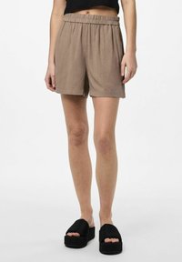 Shorts marron à taille élastique avec une coupe décontractée, présentant un tissu texturé et des ourlets roulés. Associés à des sandales noires à semelles épaisses.