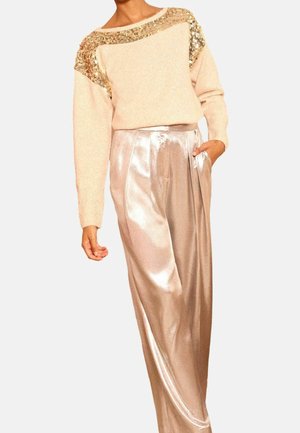 Femme portant un pull beige avec des sequins dorés sur les épaules, associé à un pantalon large taille haute couleur champagne brillant.