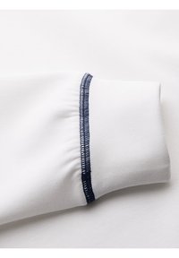 Manche en tissu blanc avec un détail élastique froncé et une couture overlock bleu marine le long du bord de la couture.