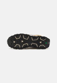 Zapatilla de trail running con suela de goma negra, patrón de agarre texturizado y acentos beige. Cuenta con un upper ligero para mayor durabilidad.