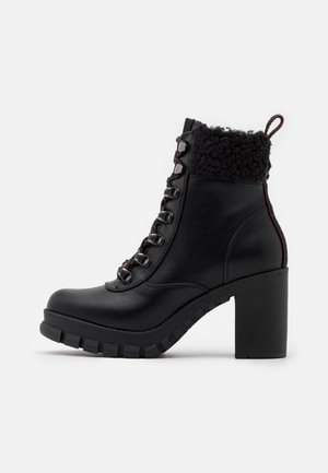 Bottine en cuir noir avec talon épais, bout arrondi, fermeture à lacets à l'avant et détail de manchette en polaire noire.