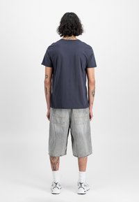 T-paita tummansinisestä puuvillasta, jossa on pyöreä kaula-aukko, yhdistettynä vaaleanharmaisiin farkkushortseihin, joissa on kaksi takataskua ja repsottava helma.