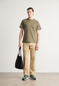 Oliven grønn bomulls T-skjorte med korte ermer, beige vide bukser, grønne sneakers og en svart totebag. Enkelt design med minimale accenter.