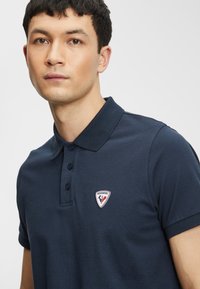 Námořnická modrá polo košile s tříknoflíkovým zapínáním a logem na levé hrudi; vyrobena z texturované bavlny.