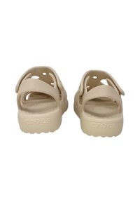 Beige Crocs sandals with two adjustable straps, round ventilation holes, and a textured footbed. Solid, cushioned sole with 'CROCS' branding.