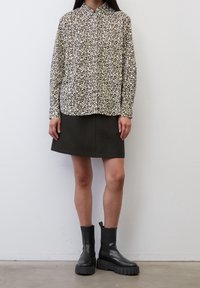 Camicia a maniche lunghe nera con pois crema abbinata a una mini gonna verde scuro e stivali neri alla caviglia con suole spesse e tacco sottile.