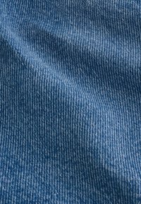 Približnji posnetek modrega denim tkanine, ki prikazuje podrobno diagonalno tkanje in subtilno senčenje zaradi gub na tkanini.