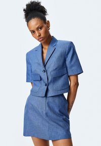 Blauwe cropped blazer met korte mouwen en twee voorkan pockets, gecombineerd met een bijpassende high-waisted minirok, gemaakt van textuur stof.
