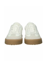 Zapatillas blancas de caña baja con punteras de ante beige, cordones blancos y suelas de goma marrón gruesas, vista frontal.