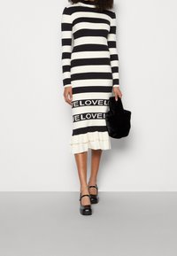 Musta-valkoisia raidoilla varustettu pitkähihaista mekkoa, jossa on röyhelöhelma ja "LOVE"-teksti alaosassa. Yhdistetty mustan pörröisen laukun ja tukevien kenkien kanssa.