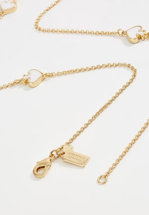 Gouden ketting met kleine open hartvormige bedels en een sluiting bevestigd aan een rechthoekig label met gravure "kate spade new york."