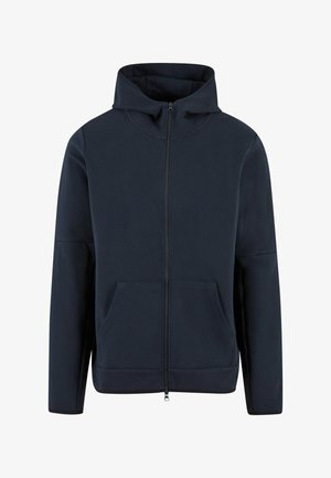 Tamsiai mėlynos spalvos užtraukiama bliuzono striukė, pagaminta iš minkštos medžiagos. Turinti aukštą apykaklę, dvi priekinės kišenes ir subtilų elastingą apvadas. Minimalistinio dizaino.