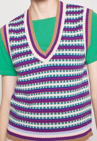 Gilet en tricot avec un col en V, présentant un motif rayé multicolore en vert, bleu, rouge et blanc, avec un col et un ourlet côtelés beiges.