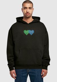 Felpa nera con cappuccio, presenta una grafica centrale di due cuori, una verde e una blu, entrambe con volti sorridenti. Tessuto morbido, tasca a marsupio.