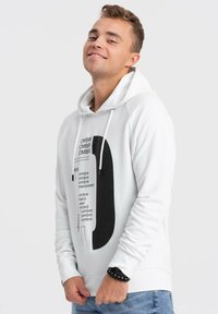 Sudadera blanca con un diseño gráfico negro, con elementos de texto y una forma redondeada. Mangas largas y capucha con cordón.