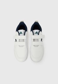 Baltos sportinės bateliai su lygiu sintetiniu viršumi, tamsiai mėlynos tekstilės pamušalu, dviem lipnia juostele ir žaliais logotipo akcentais.