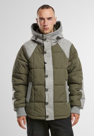 Olivengrüne Pufferjacke mit grauen Akzenten, ausgestattet mit einer durch Druckknöpfe geschlossenen Front, hohem Kragen und Seitentaschen. Strukturierter Stoff mit gestepptem Muster.