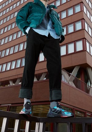 Pufferjacka i teal, blå skjorta med knappar, svarta manchesterbyxor och flerfärgade sneakers med svarta, blå och röda detaljer.
