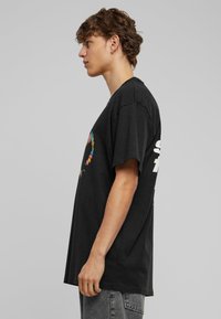 Camiseta de algodón negra de corte holgado, con un gráfico multicolor y texto blanco en la parte posterior. Textura suave y mangas cortas.