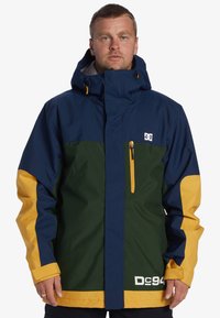 Chaqueta bloqueada en color con paneles en azul marino, verde y amarillo. Fabricada con material resistente al agua, con un alto cuello y un bolsillo con cremallera.