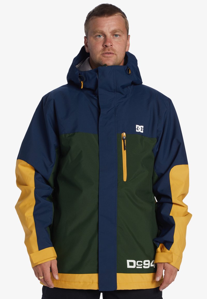 Chaqueta bloqueada en color con paneles en azul marino, verde y amarillo. Fabricada con material resistente al agua, con un alto cuello y un bolsillo con cremallera.