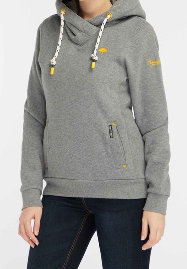 Personne portant un sweat à capuche gris avec des cordons blancs et un logo parapluie jaune, associé à un jean bleu foncé.