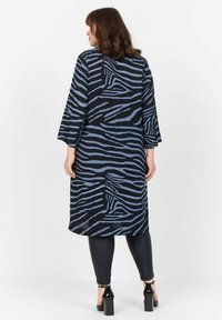 Sinine ja must zebra-mustriga tunika, millel on kolmveerand varrukad ning lõdva kärbiga, millele on sobitatud mustad legginsid ja plokkninalised kingad.