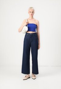 Zila strapless blusa, augsti vidukļa tumši džinsi ar platu kāju, gaišas krāsas somiņa un bēša dzīvokļi ar krustveida siksnām. Gludas tekstūras.