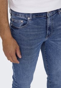 Slim-fit farkut sinisessä denimissä, jossa on tekstuuri. Varustettu viidellä taskulla ja metallinappikoristeilla vyötäröllä.