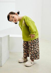 Zielona bluza z nadrukiem, zestawiona z beżowymi spodniami w szerokie nogawki w leopardzi wzór i puszystymi, kremowymi klapkami.