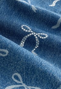 Blå denimtyg med ett ljust mönster av rosetter, prytt med små strasstenar, som visar en texturerad yta och mjuk fall.