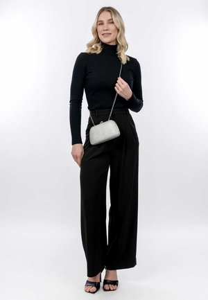Black ribbed turtleneck, high-waisted black pleated trousers, and black open-toe heels. Holding a silver textured clutch with chain strap.