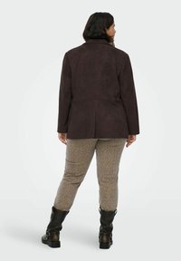 Pruun kunstsuede jakk, millel on kohandatud lõige, koos beežide pükstega, millel on õrn leopardimuster ja mustad põlvikud.