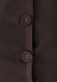 Tmavě hnědá látka s dvěma kulatými knoflíky se stříbrným kováním, umístěná na texturovaném povrchu se šitím.