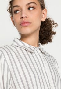 Shirt featuring vertical gray and white stripes, collared design, soft texture, and button closures. Visible stitching along collar.