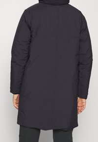 Lång, mörkgrå pufferjacka med hög krage, jämn textur, centrerad bakseam och långa ärmar, som sträcker sig till mid-lår längd.