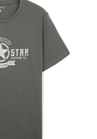 T-shirt in cotone grigio con maniche corte, collo rotondo e una grafica stampata a tema motociclistico in bianco scolorito. L'etichetta riporta "STAR CLOTHING CO."