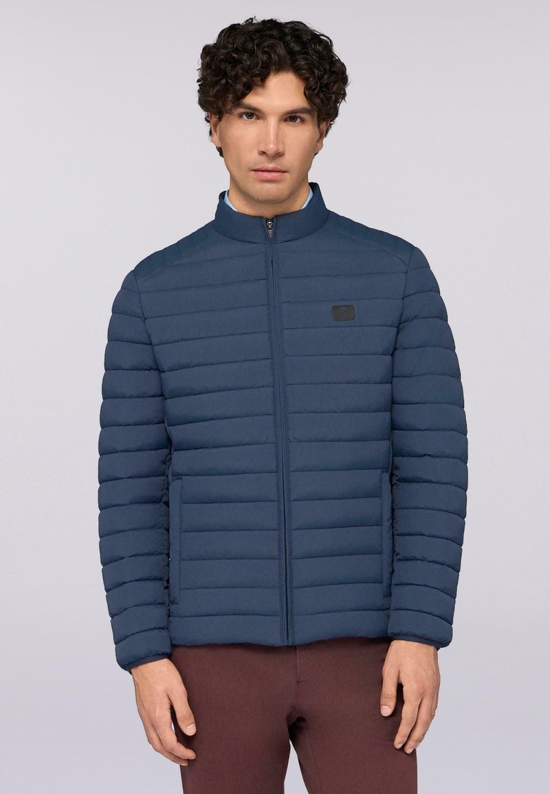 Marinblå puffjacka med horisontell sömnad, hög krage och framfickor med dragkedja. Har en liten logotyp på bröstet, tillverkad av lätt material.