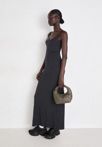 Long, fitted black dress with thin straps, textured olive green handbag, and chunky black sneakers. Smooth fabric, body-hugging design.
