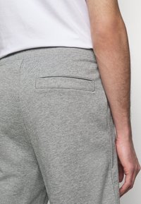 Pantalons de survêtement gris avec une texture lisse, dotés d'une poche arrière et d'une taille élastique. Le tissu semble doux et décontracté.