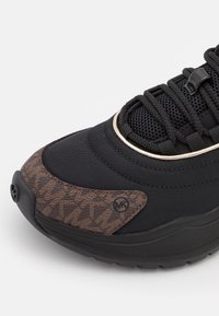 Baskets noires avec bout en cuir marron texturé, lacets noirs, languette en mesh et semelle, avec un logo circulaire MK sur la zone du bout.