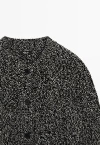 Cardigan in maglia bianco e nero con motivo a trecce testurizzato, collo alto e tre bottoni neri sul davanti.