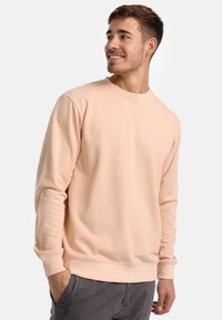 Lyserød crewneck sweatshirt i blødt stof, med lange ærmer og ribbede manchetter, parret med grå bukser. Simpelt design, uden mønstre.