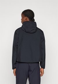 Black waterproof jacket with a hood, featuring a cropped design and elastic cuffs. Smooth texture and minimal branding on the back.