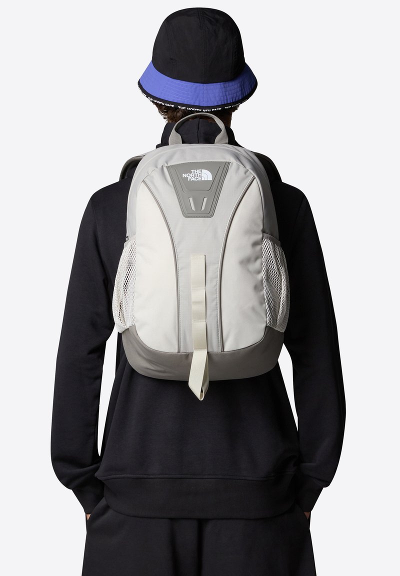 Zaino grigio e beige con spallacci imbottiti, tasche laterali in rete e un logo sul davanti. Tessuto liscio e resistente con una forma strutturata.