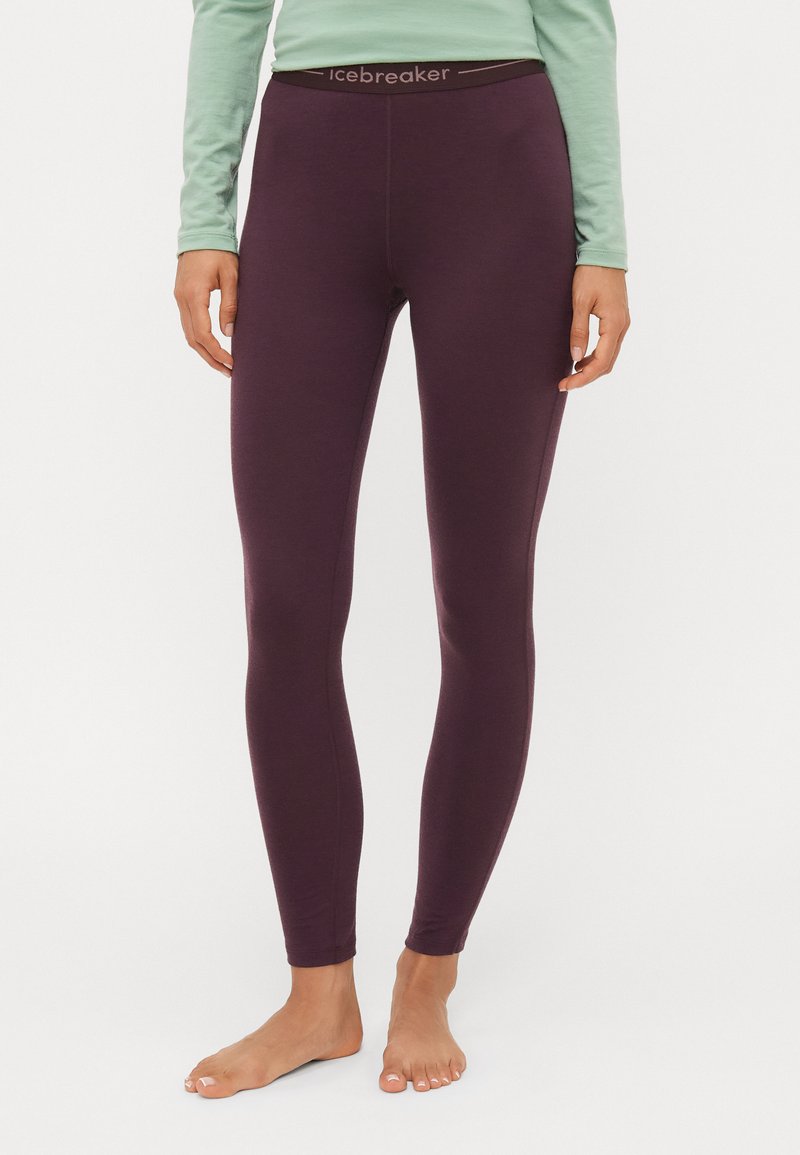 Lilla leggings laget av mykt, stretchy materiale med en bred svart midjebånd som har "Icebreaker"-logoen. Glatt tekstur og full lengde.