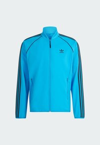 Giacca da jogging blu con zip, strisce nere sulle maniche, colletto alto e logo sul petto. Realizzata in materiale liscio e leggero.
