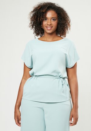 Top azzurro chiaro con vestibilità morbida, maniche corte e dettaglio del punto vita annodato. Tessuto liscio con una consistenza morbida, abbinato a pantaloni coordinati.